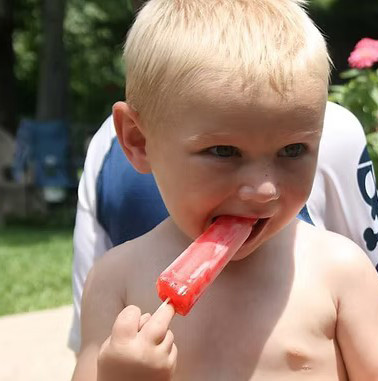 A young child is enjoying a red popsicle while standing outdoors.