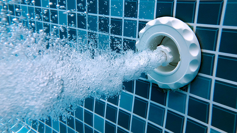Water bubbles flowing from a jet in a tiled swimming pool.