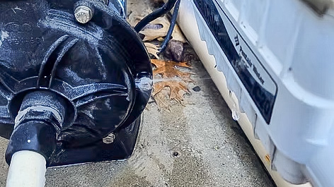 A close-up of a water pump next to a white container, with some dry leaves on the ground.