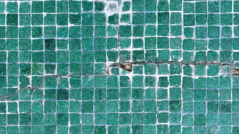 A close-up of green mosaic tiles arranged in a grid pattern, with some visible cracks.