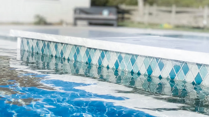 A close-up view of a swimming pool edge with a patterned tile border, reflecting water ripples.