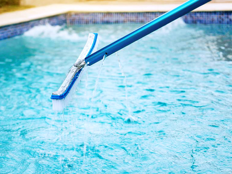 A pool skimmer is submerged in water, removing debris while water splashes off the edges.